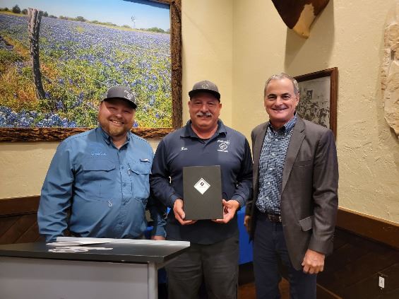 Three people standing and smiling at a camera. One holds a certificate.